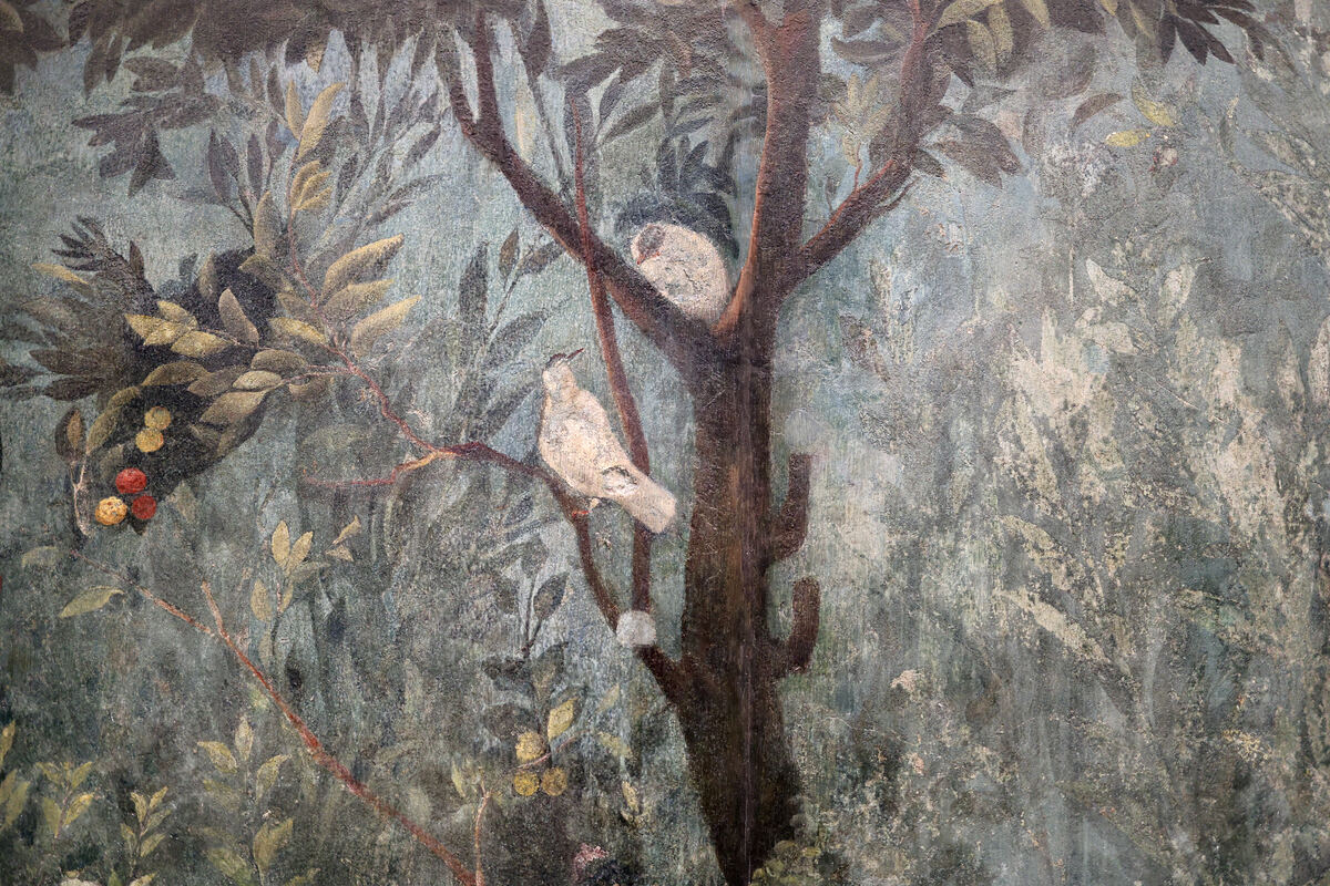 A Roman wall painting of a garden: a pale bird on a branch and another in the fork of a tree, among leaves and small red and yellow fruit.