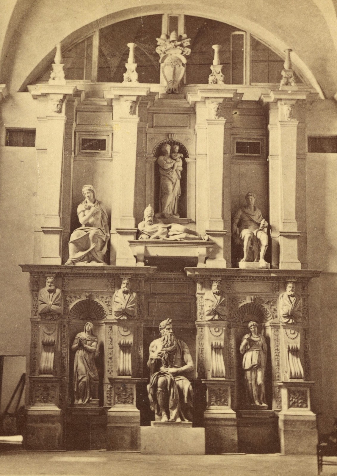 An old photograph of the finished tomb of Julius II: a two-story marble wall with Moses seated at the bottom center between two standing women, and four more figures above.
