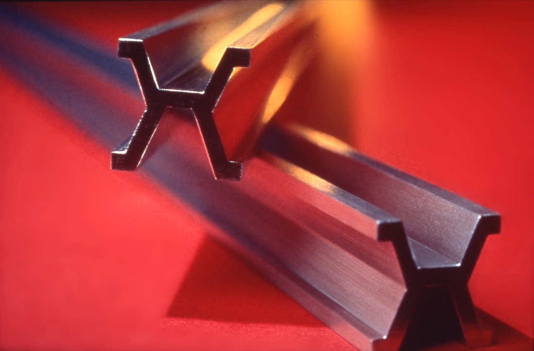 Two platinum-iridium meter bars on a red surface, seen end on, so their X-shaped cross-sections show.