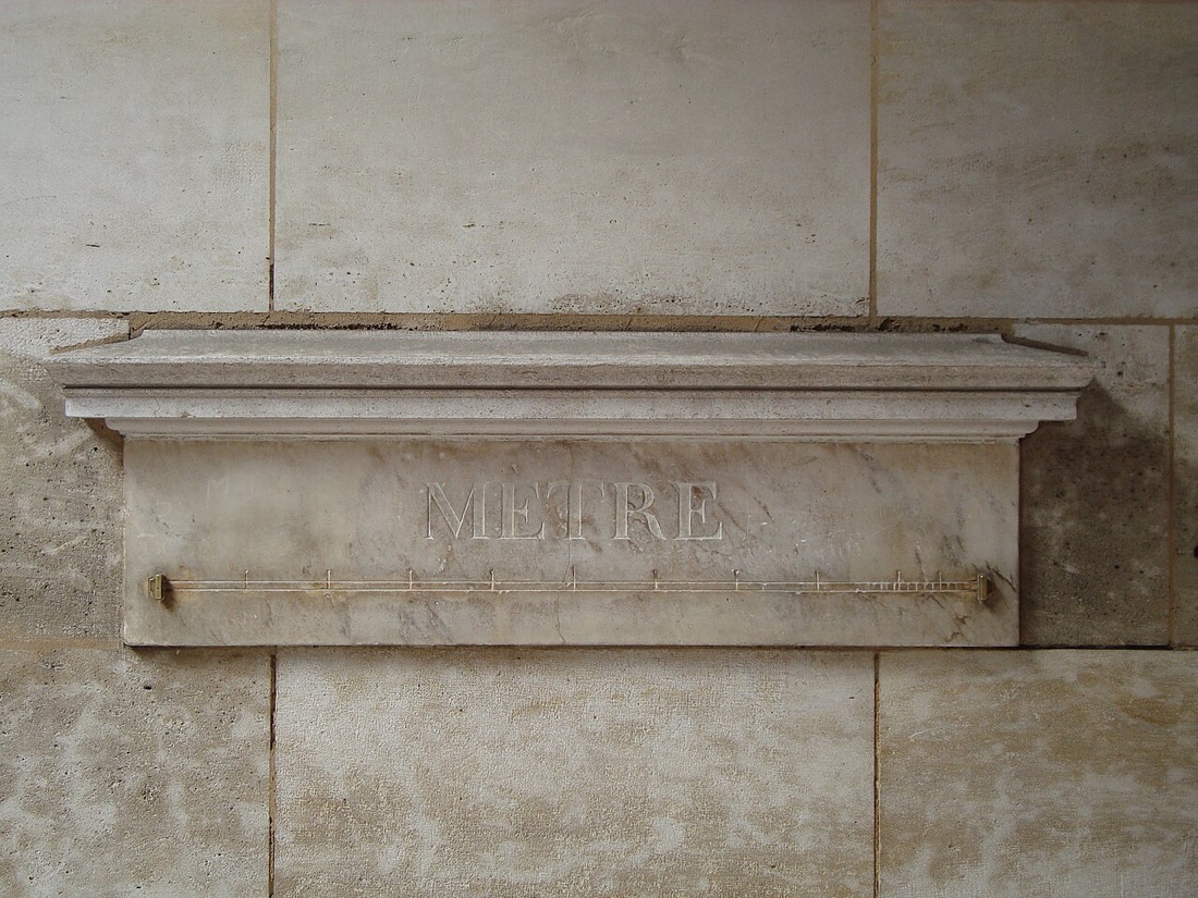 A marble standard meter set into a stone wall in Paris, with the word MÈTRE carved above a brass rule and a marble shelf over it.